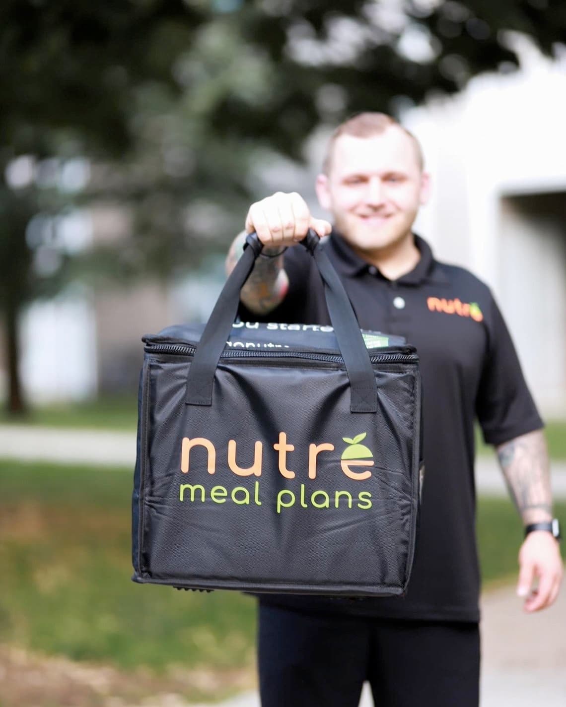 Person carrying black Nutre branded delivery bag.